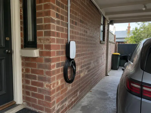 Wall-mounted EV charger and coiled cable on a brick exterior wall beside a narrow driveway in Marrickville