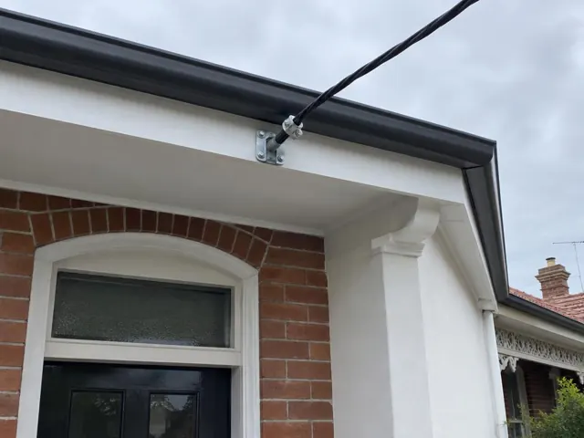 Overhead service cable and point-of-attachment bracket on a brick house exterior in Tempe